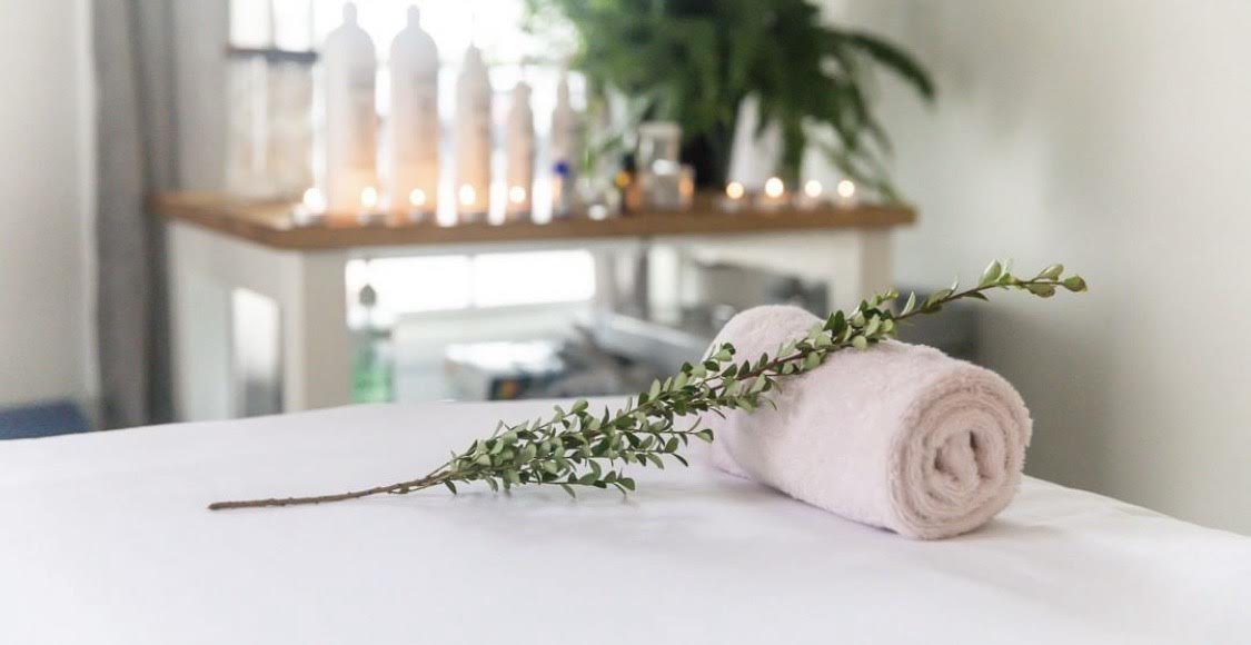 Rolled towel with green branch on white table in a spa setting.