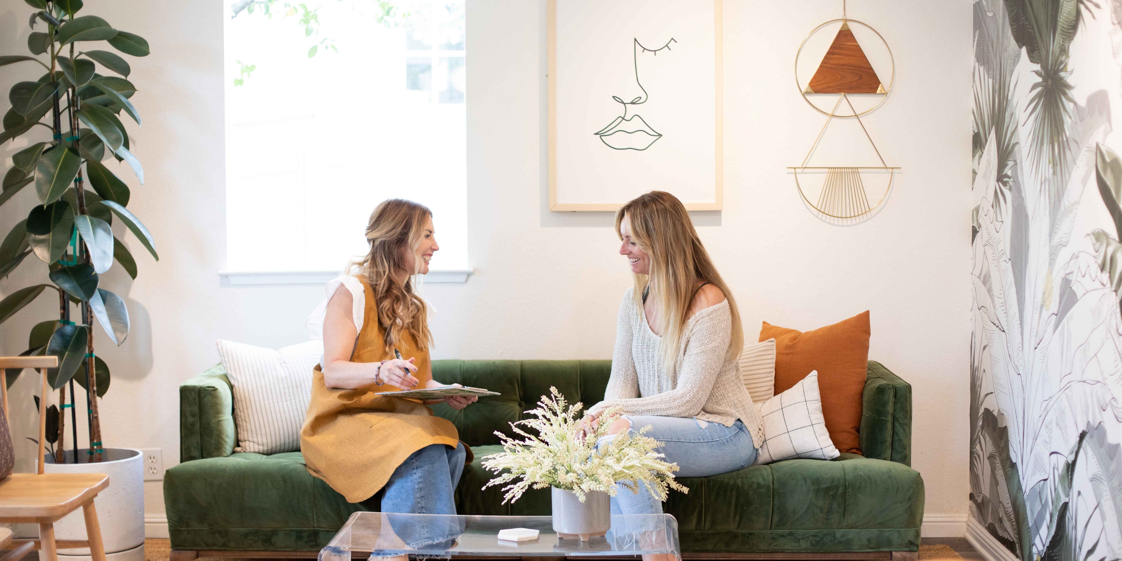 Two women sitting on a green couch in a stylish room.