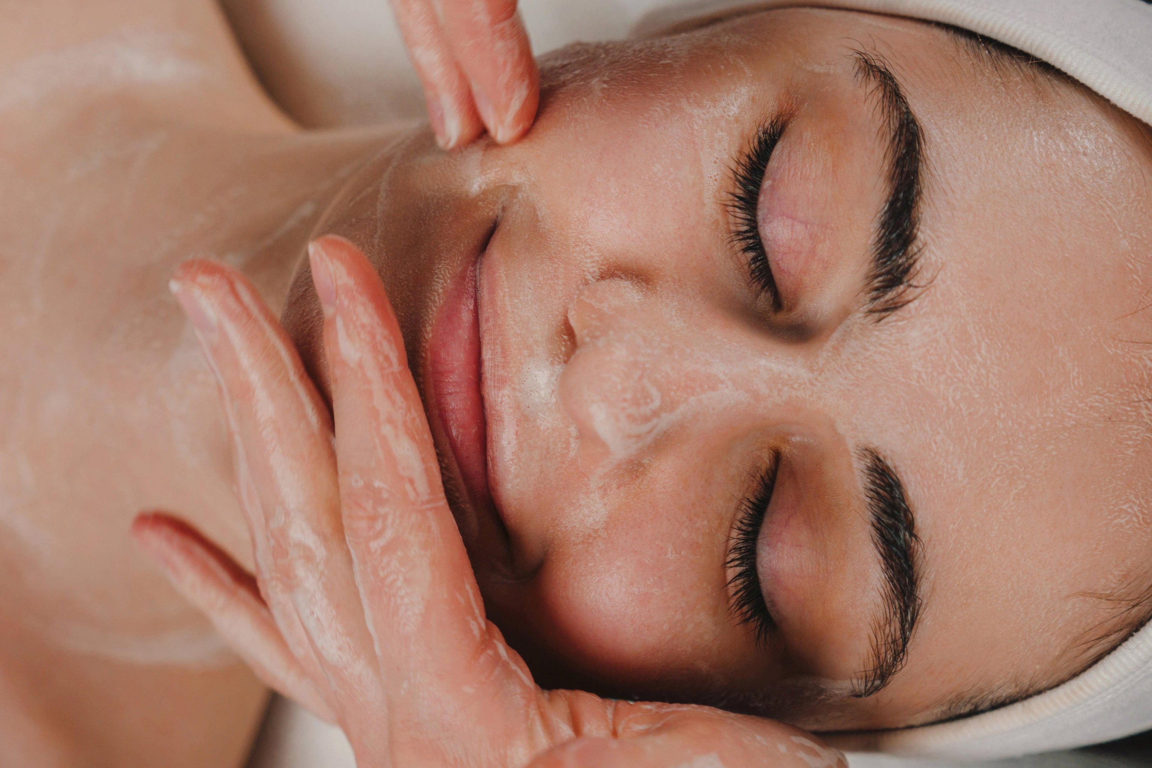 Close-up of a person receiving a facial massage with hands applying cream to the face.